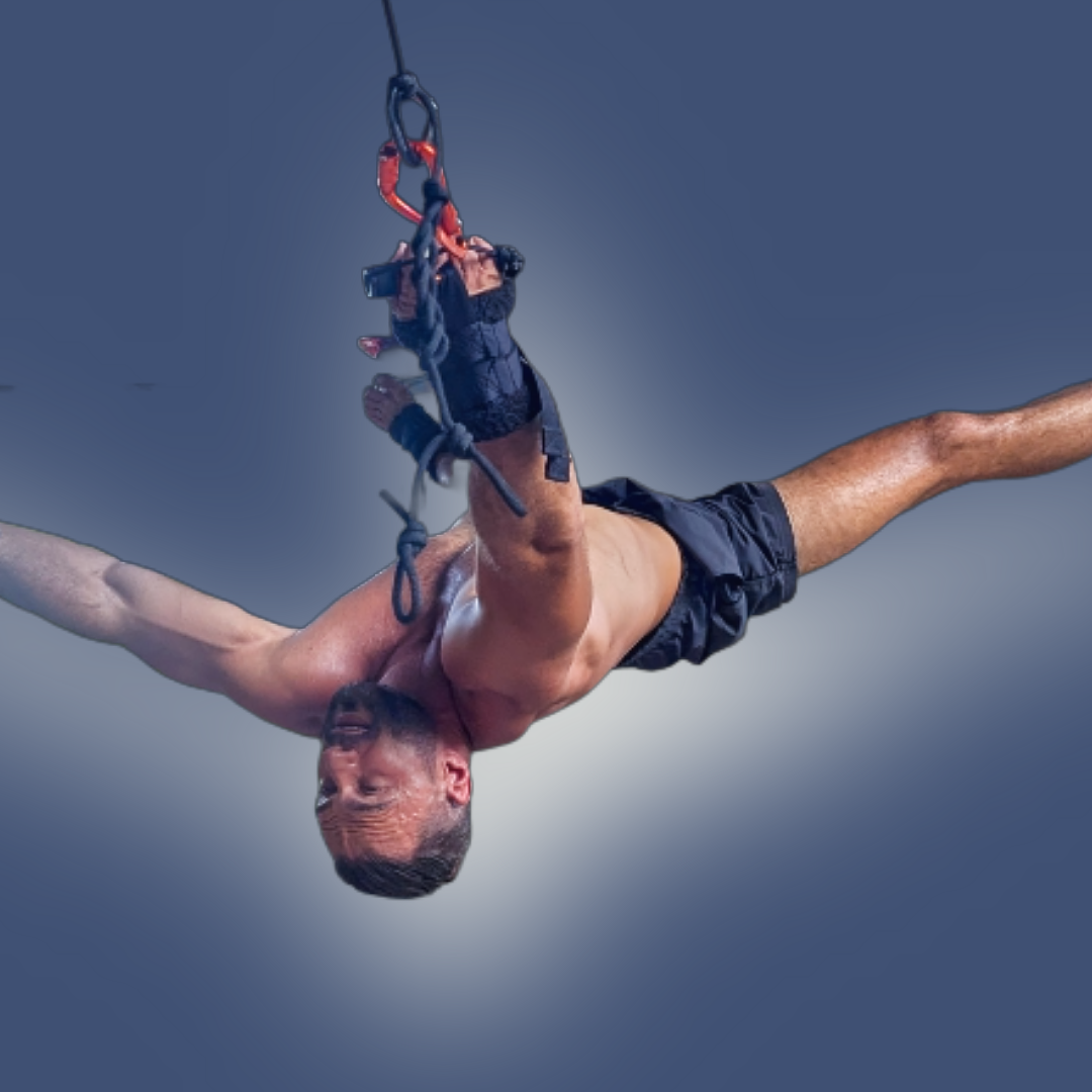 A man performing Pravilo decompression therapy, suspended with arms outstretched while looking down in a deep stretch.
